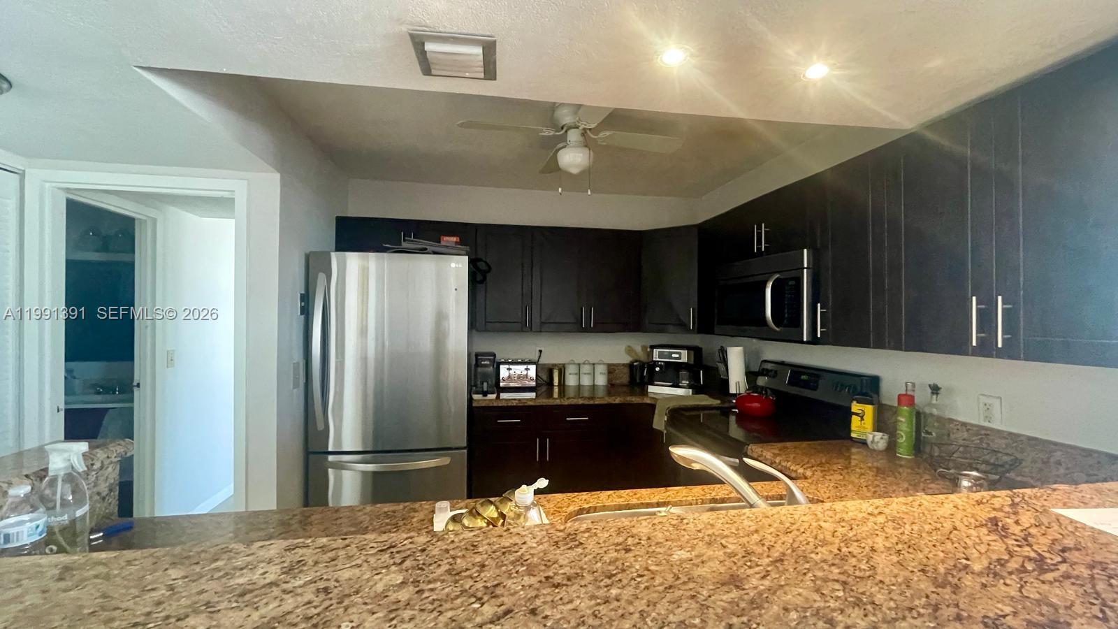 A kitchen features dark wood cabinets, stainless steel appliances, and brown granite countertops — 2017 OCEAN DR # 405W, Hallandale Beach FL 33009, HALLANDALE BEACH, FL