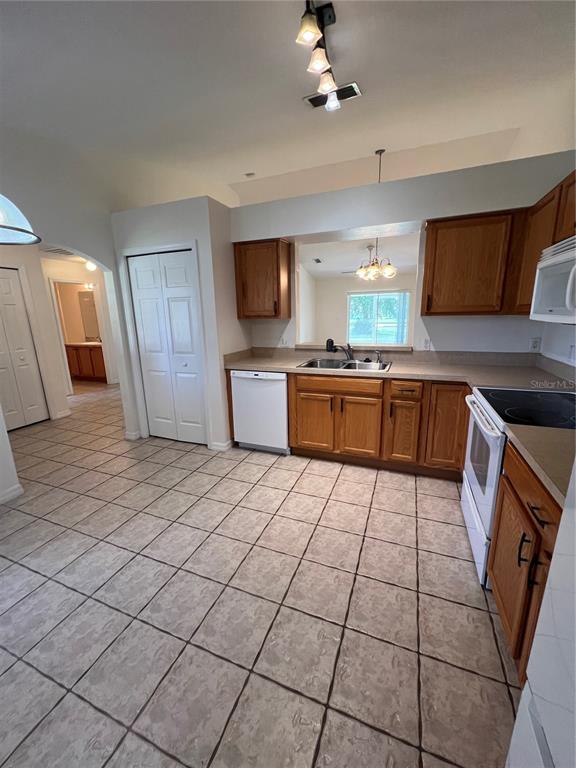 A kitchen features wood cabinets, tile flooring, a white dishwasher, and a pass-through window — 3364 CELENA CIRCLE, ST CLOUD, FL