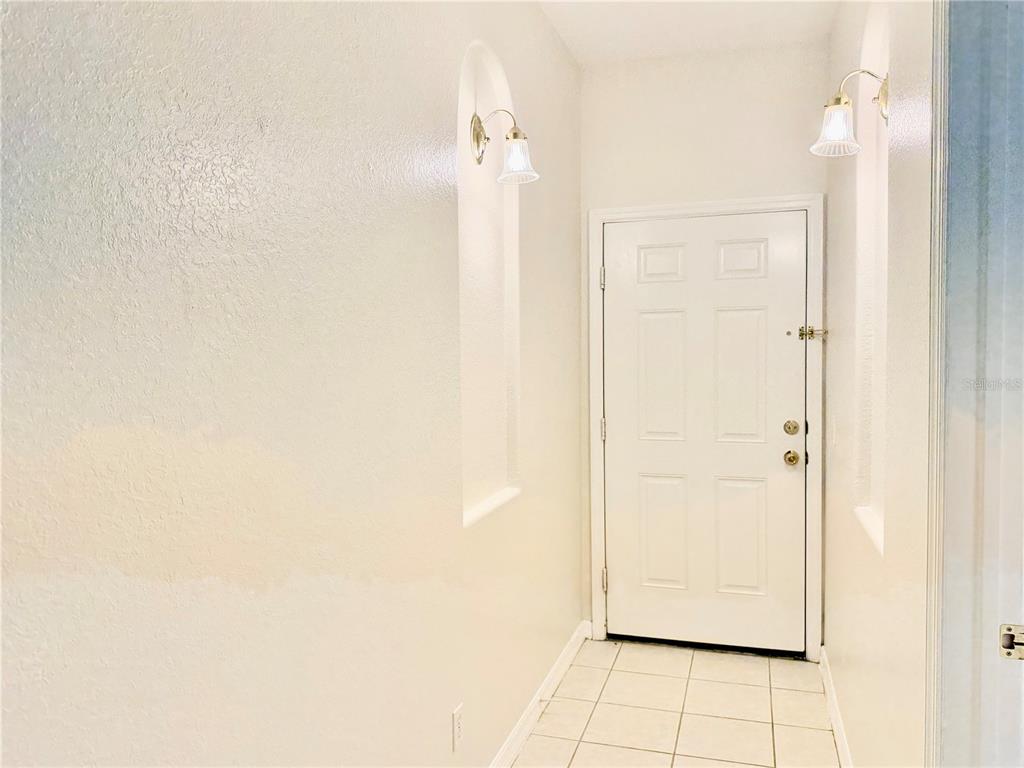 A tiled entryway features a white door flanked by two arched wall niches with sconces — 819 FAIRWAYCOVE LANE UNIT 102, BRADENTON, FL