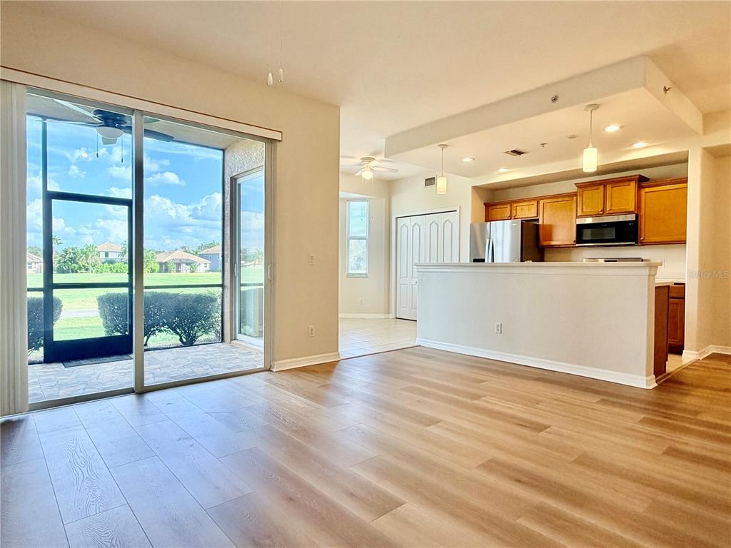 A living room with wood-look flooring opens to a kitchen and a screened-in patio — 819 FAIRWAYCOVE LANE UNIT 102, BRADENTON, FL