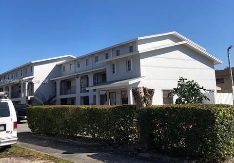 A multi-story white apartment building stands behind a manicured green hedge under a clear sky — 1460 N 43rd Pl # 106, Hialeah FL 33012, HIALEAH, FL