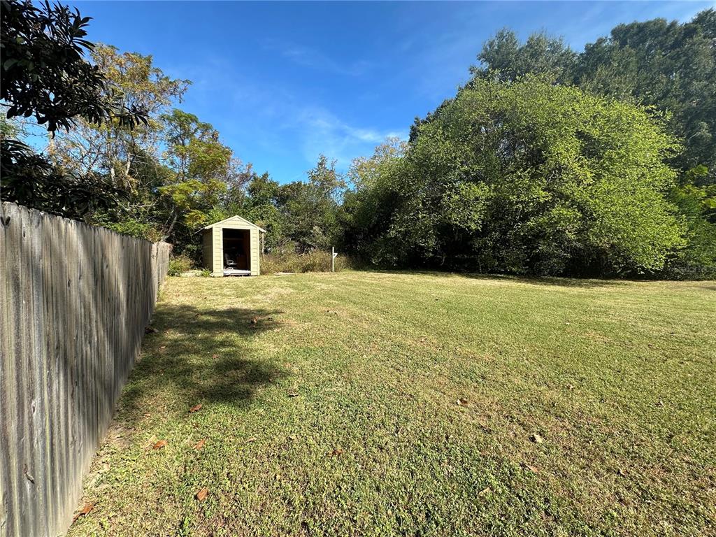 A grassy backyard features a wooden fence on the left and a small storage shed — TBD NW 125TH PLACE, CITRA, FL
