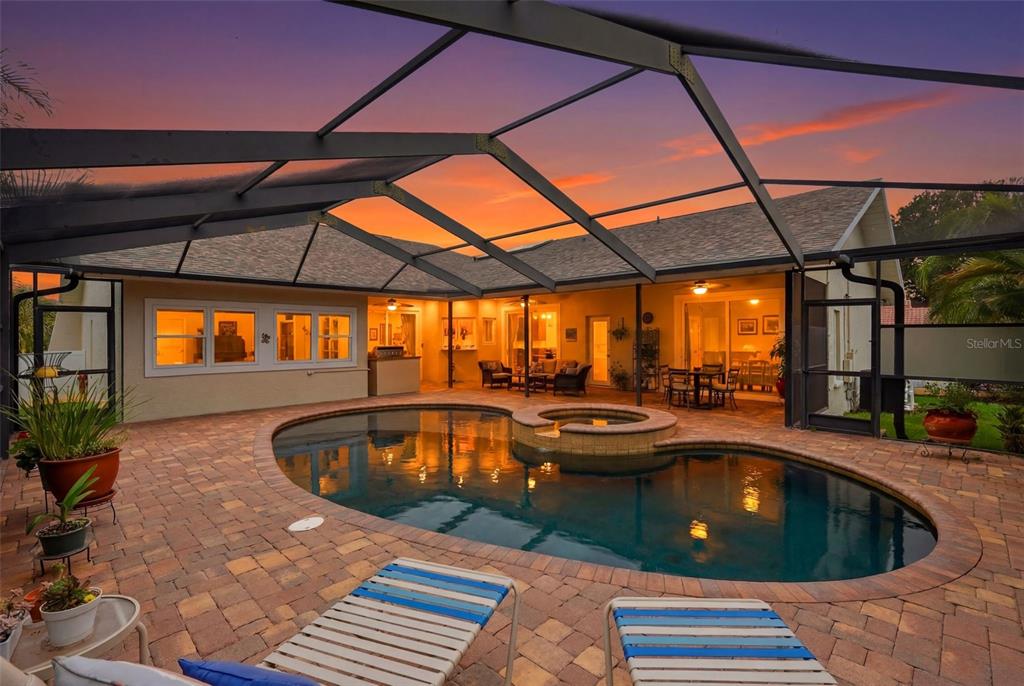 A screened-in patio features a swimming pool, a hot tub, and brick pavers at sunset — 661 7TH AVENUE N, TIERRA VERDE, FL