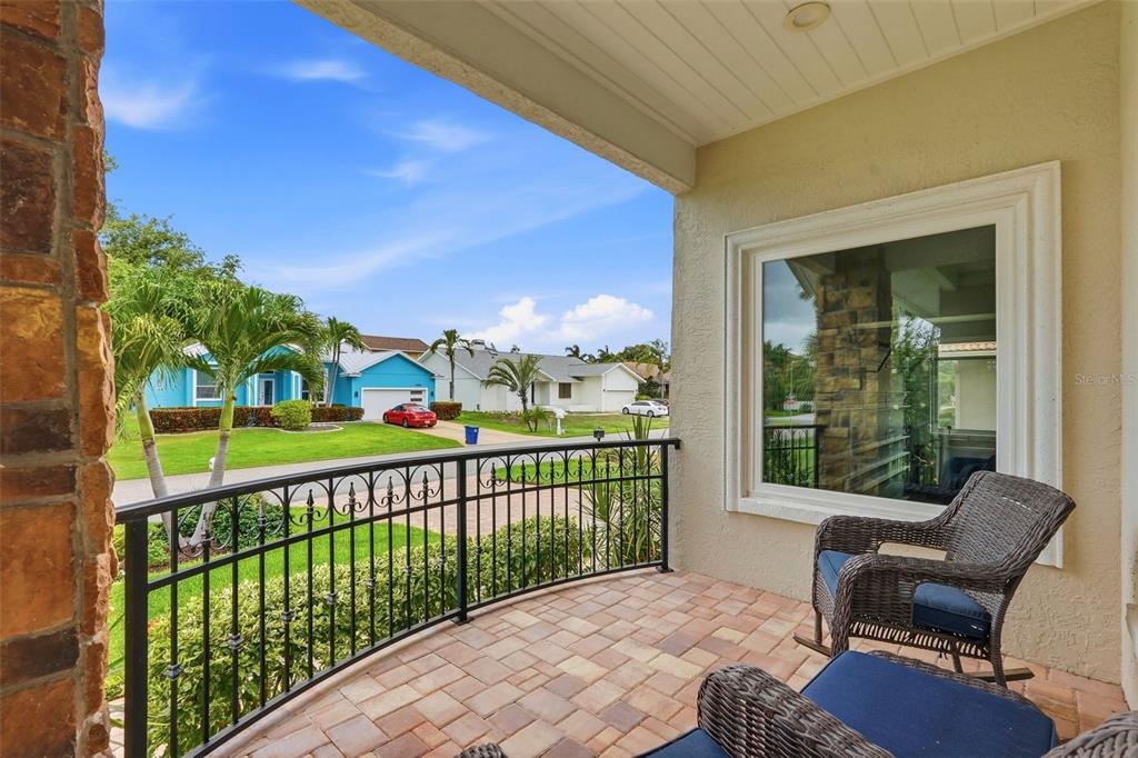 A covered balcony features a paver floor, black metal railing, and outdoor seating — 661 7TH AVENUE N, TIERRA VERDE, FL