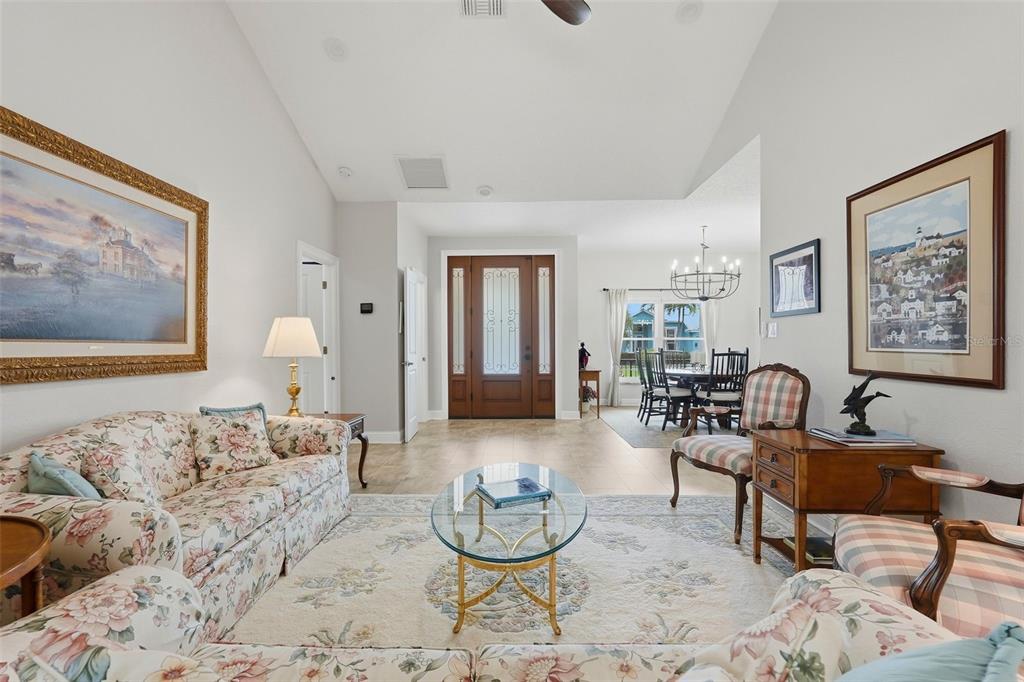 A living room with floral sofas, a glass coffee table, and a view of the entryway — 661 7TH AVENUE N, TIERRA VERDE, FL