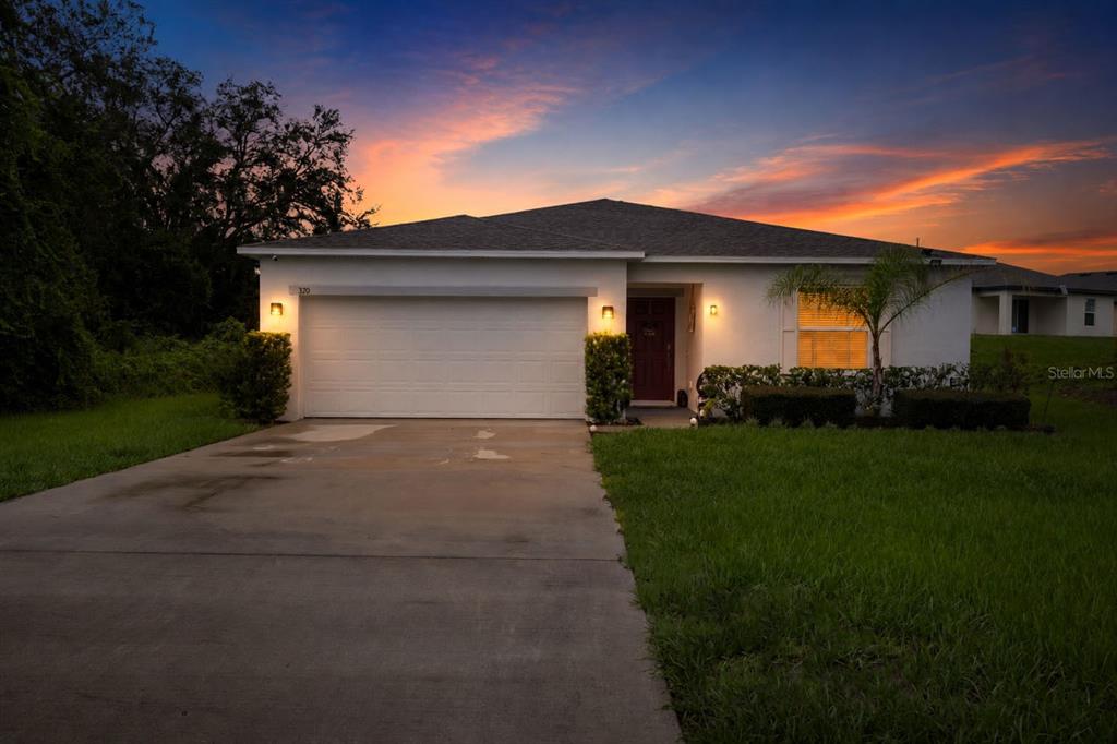 A single-story house with a white exterior, a two-car garage, and a sunset sky — 320 ST CLOUD ROAD, POINCIANA, FL