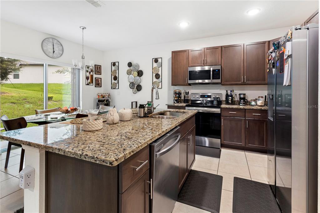 A kitchen features dark wood cabinets, granite countertops, stainless steel appliances, and a dining area — 320 ST CLOUD ROAD, POINCIANA, FL