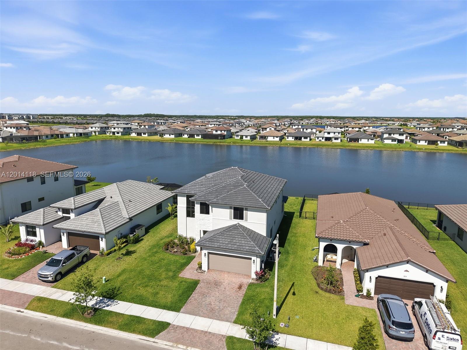 An aerial view shows three suburban houses with tiled roofs situated along a large lake — 5023 OFANTO, Ave Maria FL 34142, AVE MARIA, FL