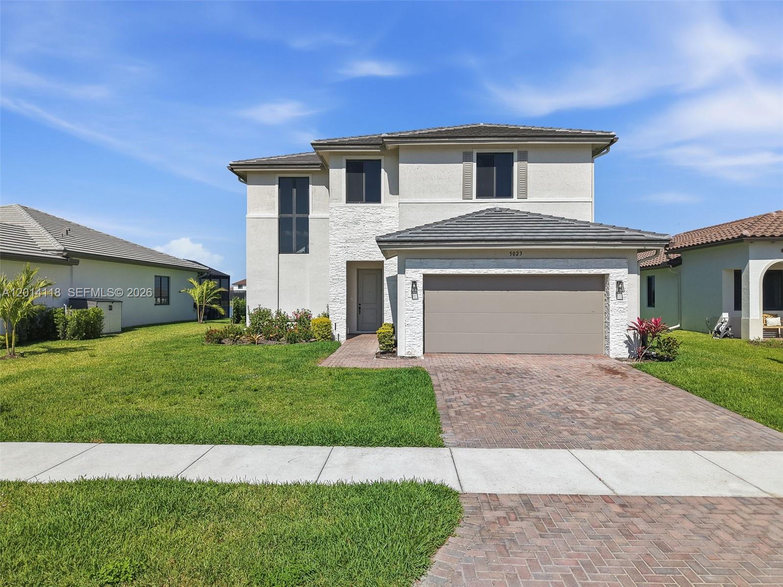 A two-story house with a beige stucco exterior, stone accents, and a brick driveway — 5023 OFANTO, Ave Maria FL 34142, AVE MARIA, FL