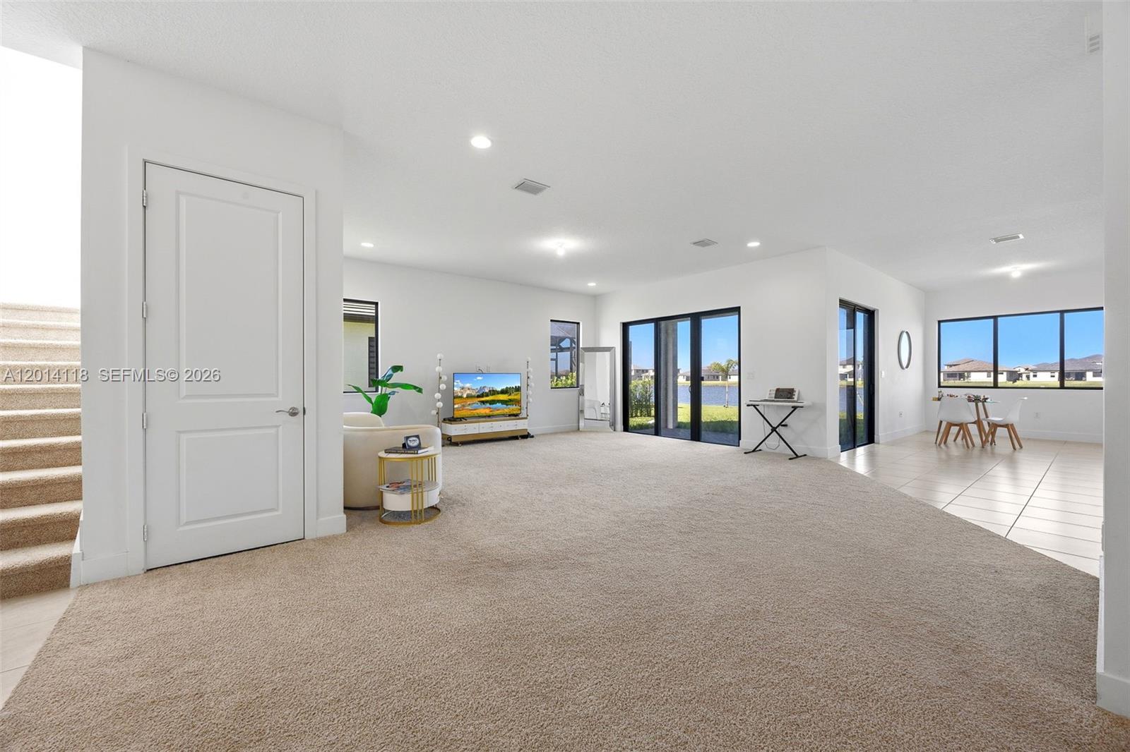 A spacious living area features beige carpeting, white walls, large windows, and a sliding glass door — 5023 OFANTO, Ave Maria FL 34142, AVE MARIA, FL