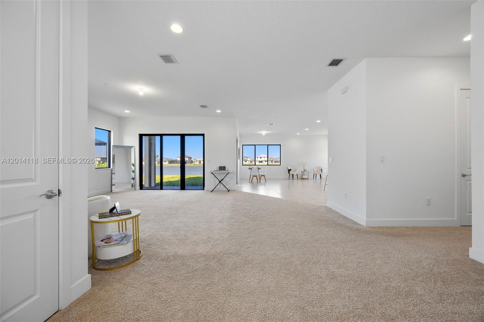 A spacious, open-concept living area features beige carpeting, white walls, and large glass sliding doors — 5023 OFANTO, Ave Maria FL 34142, AVE MARIA, FL