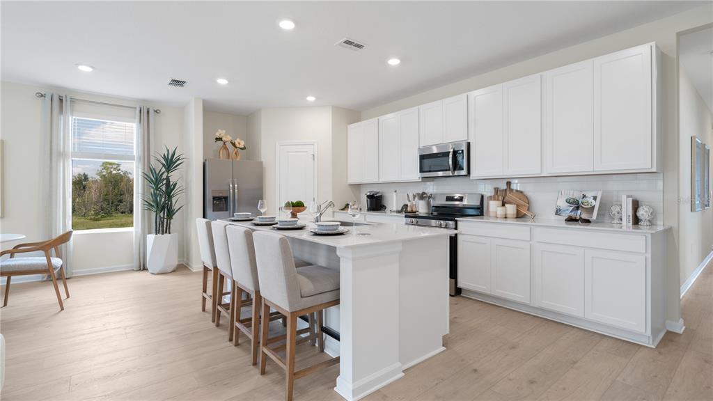 A modern kitchen features white cabinetry, a central island with bar seating, and light flooring — 3141 ROCKWOOD WAY, MINNEOLA, FL