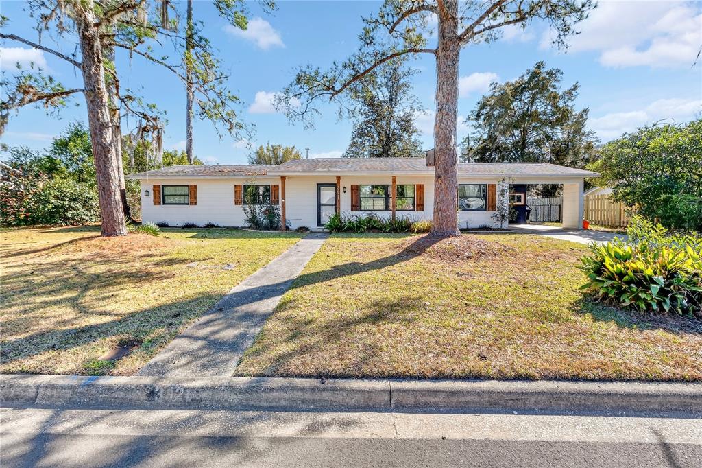 A single-story house with white siding, wood shutters, and a carport under a blue sky — 3321 NW 28TH PLACE, GAINESVILLE, FL