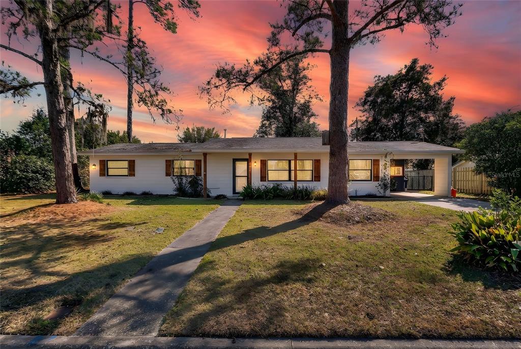 A single-story white house with a carport and a walkway sits under a sunset sky — 3321 NW 28TH PLACE, GAINESVILLE, FL