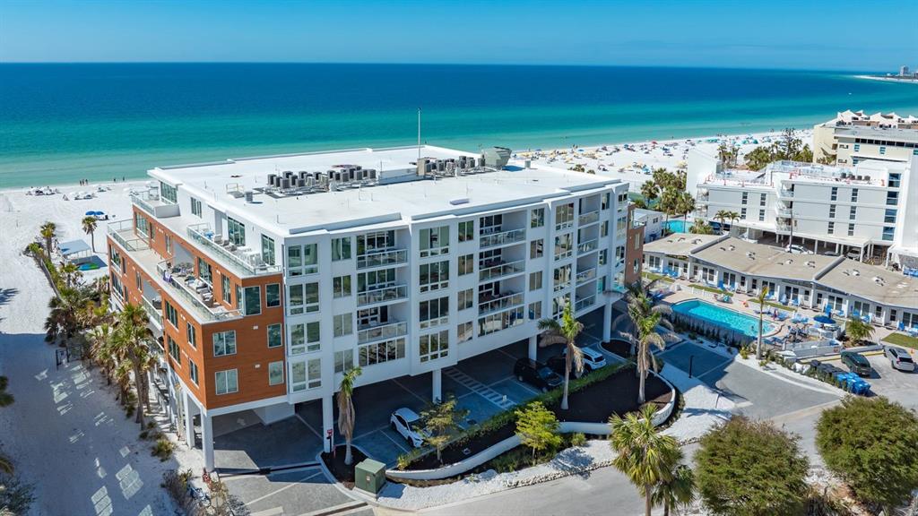 An aerial view shows a modern multi-story beachfront condominium building with parking underneath — 1035 SEASIDE DRIVE UNIT 503, SARASOTA, FL