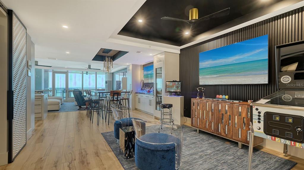 A modern game room features a large television, pinball machine, bar area, and blue seating — 1035 SEASIDE DRIVE UNIT 503, SARASOTA, FL