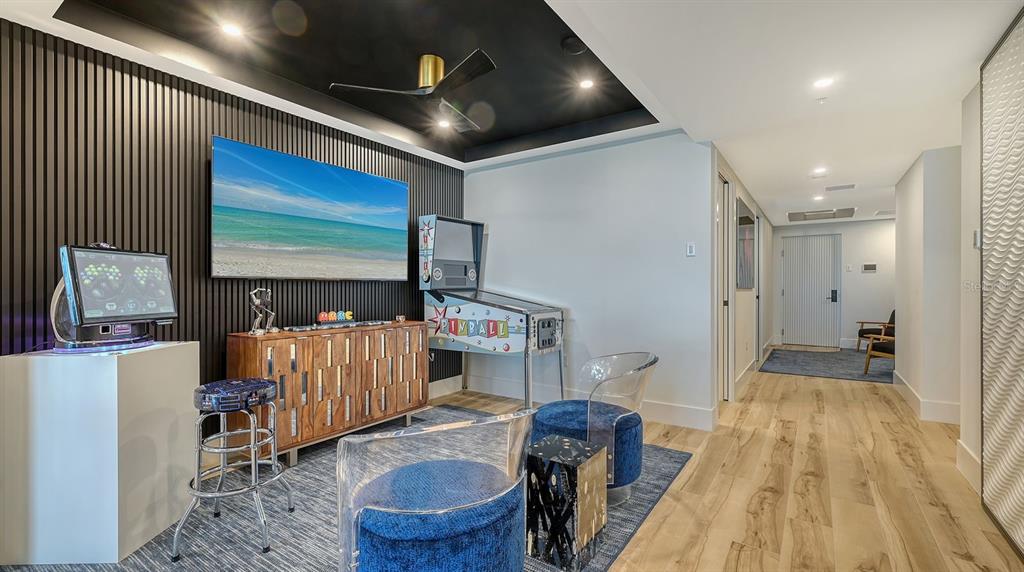 A game room features a pinball machine, a wall-mounted television, and modern blue seating — 1035 SEASIDE DRIVE UNIT 503, SARASOTA, FL