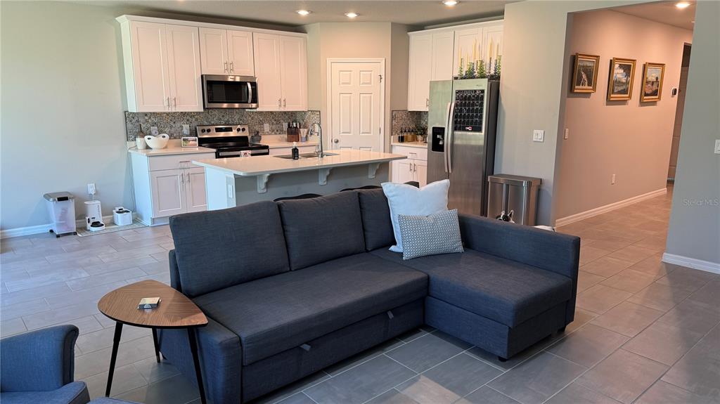 A kitchen with white cabinets and a stainless steel refrigerator overlooks a grey sectional sofa — 17241 CAGAN CROSSINGS BOULEVARD, CLERMONT, FL