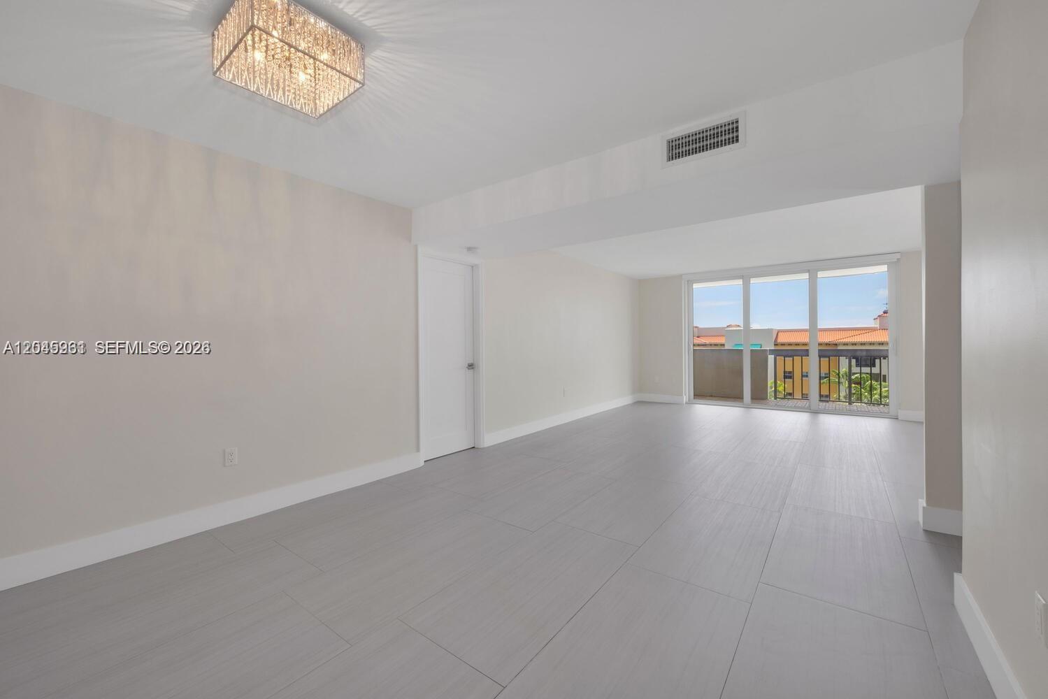 An empty room features light gray tile flooring, a crystal ceiling fixture, and a balcony view — 600 Biltmore Way # 618, Coral Gables FL 33134, CORAL GABLES, FL