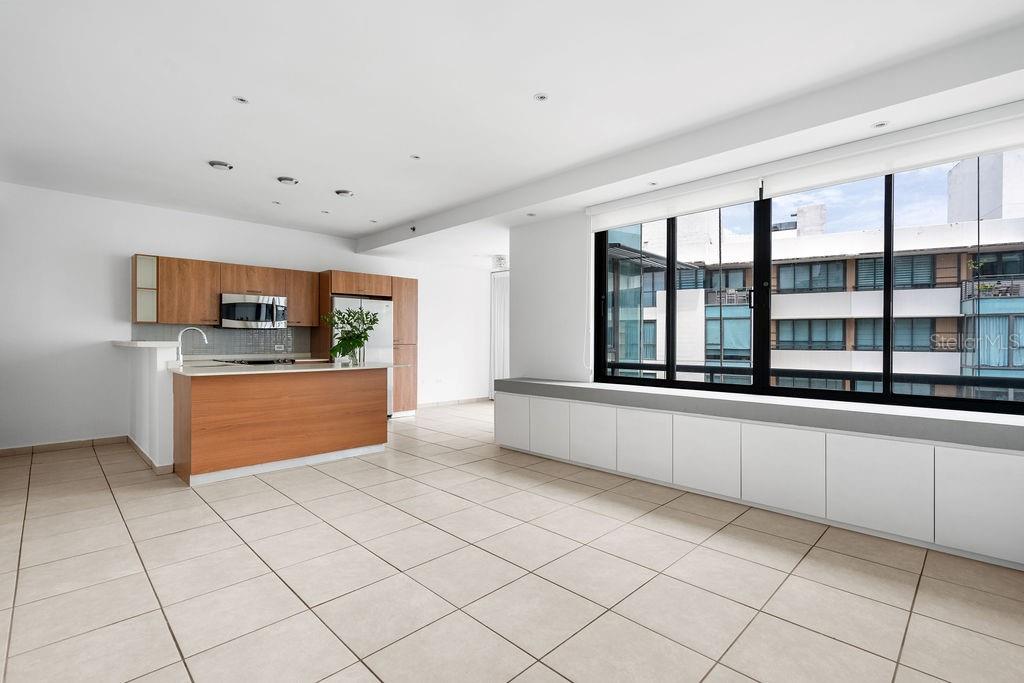 A kitchen with wood cabinets and a breakfast bar opens into a living area with windows — 1511 PONCE DE LEON AVENUE UNIT 473, SAN JUAN, PR