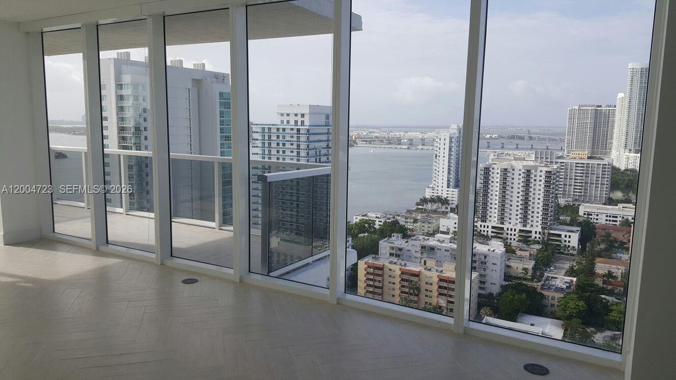 An empty room with floor-to-ceiling windows overlooks a city skyline and a body of water — 600 NE 27th St # 2705, Miami FL 33137, MIAMI, FL