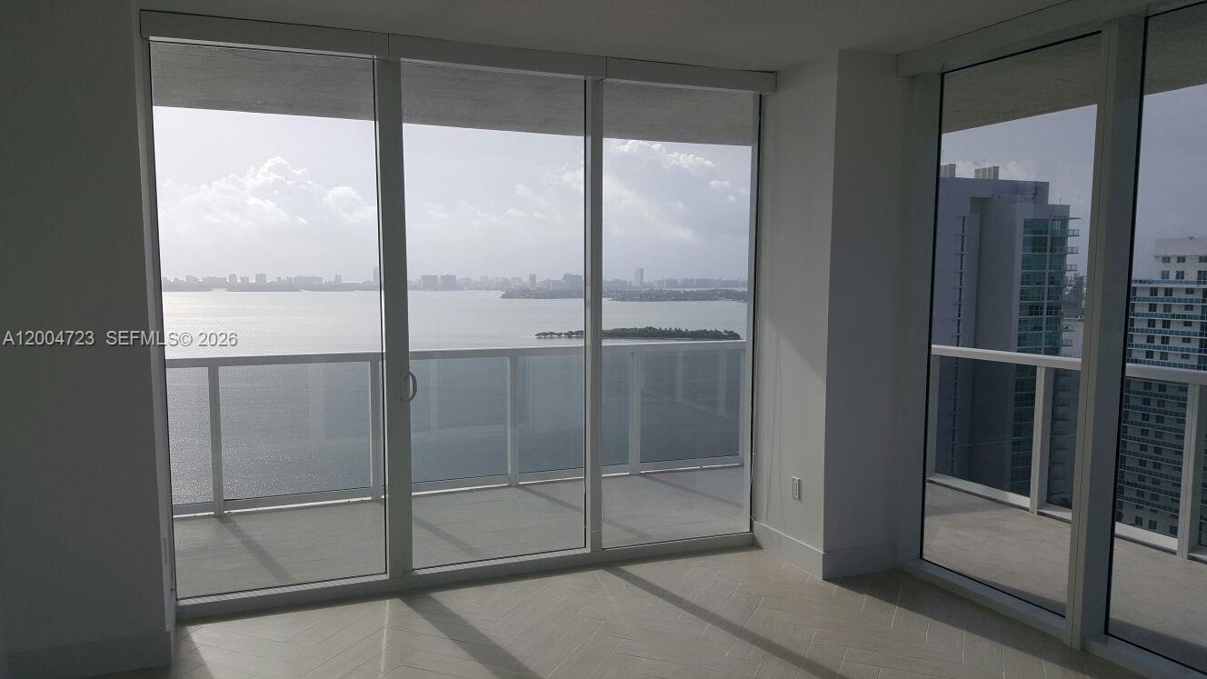 A room with floor-to-ceiling windows overlooks a balcony, a bay, and city buildings — 600 NE 27th St # 2705, Miami FL 33137, MIAMI, FL