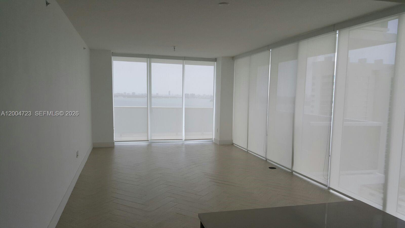 An empty room features light-colored herringbone wood floors and floor-to-ceiling windows with roller shades — 600 NE 27th St # 2705, Miami FL 33137, MIAMI, FL