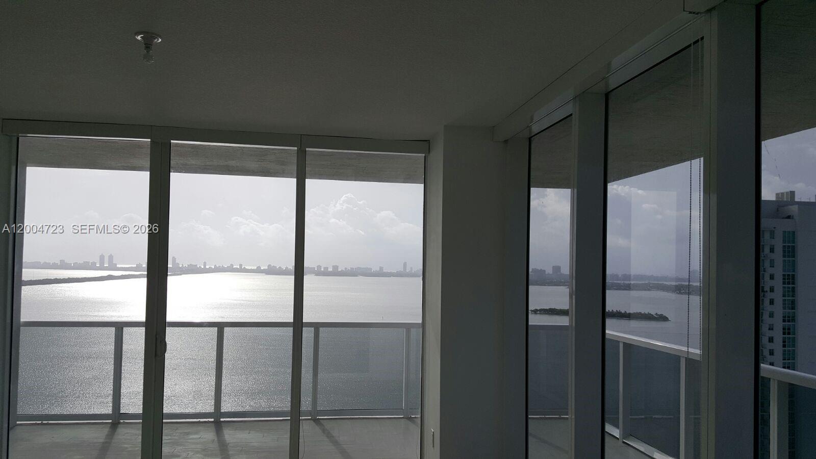 A room with floor-to-ceiling windows overlooks a large body of water and a city skyline — 600 NE 27th St # 2705, Miami FL 33137, MIAMI, FL