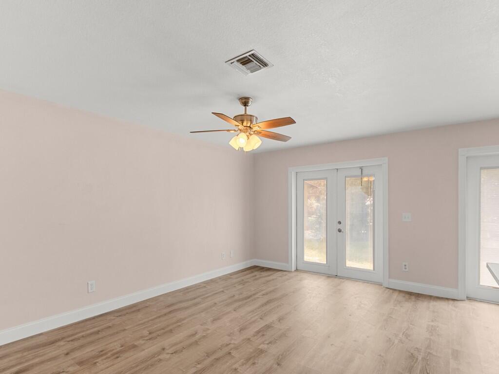 An empty room with light pink walls, wood-look flooring, a ceiling fan, and French doors — 4065 46th Lane, Vero Beach FL 32967, VERO BEACH, FL