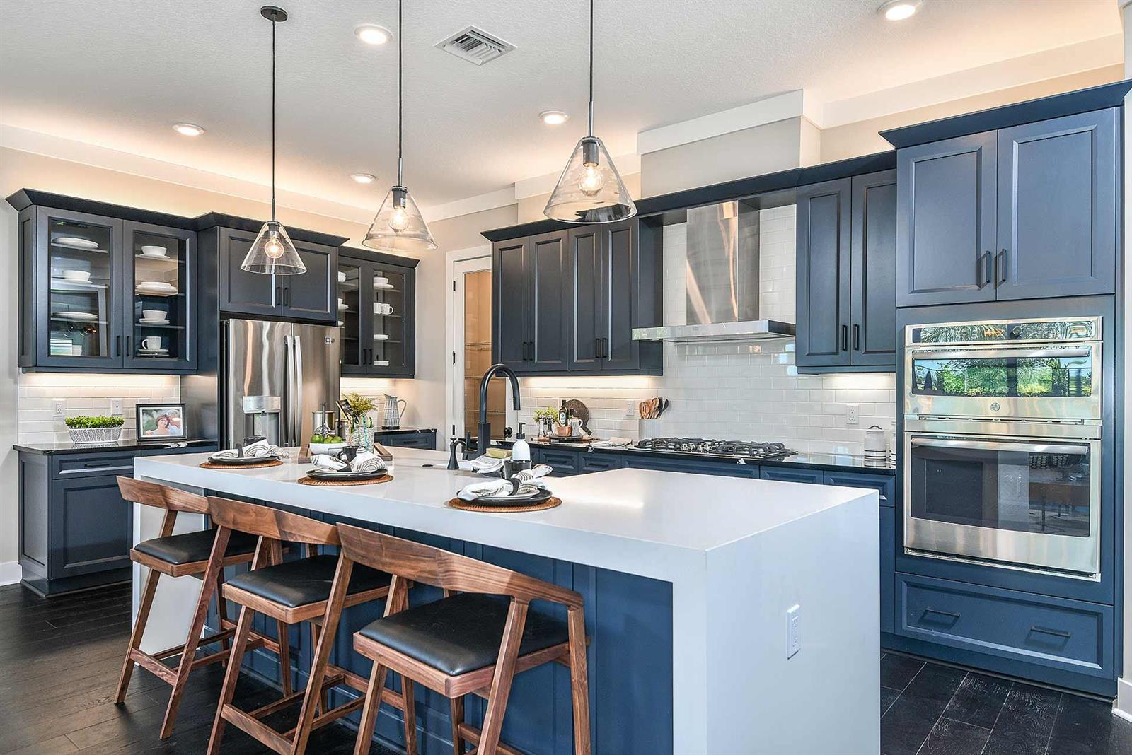 A kitchen features dark blue cabinets, a white waterfall island, and three glass pendant lights — 5633 Saint Armands Way, Westlake FL 33470, WESTLAKE, FL