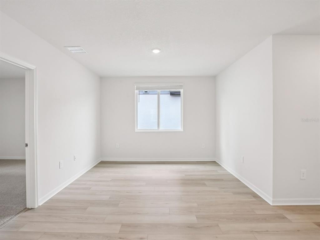 An empty room with light-colored walls, wood-look flooring, a single window, and a doorway — 10436 ABUNDANCE GROVE WAY, PARRISH, FL
