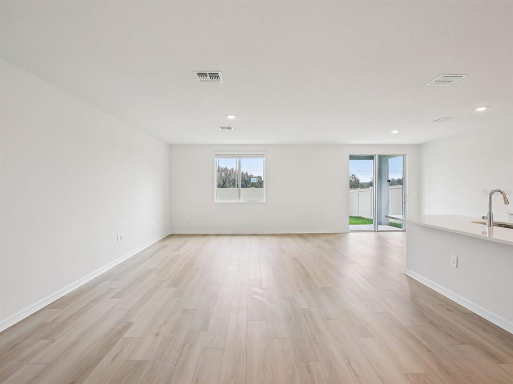 An open-concept living area features light wood-look flooring, white walls, a window, and sliding doors — 10436 ABUNDANCE GROVE WAY, PARRISH, FL
