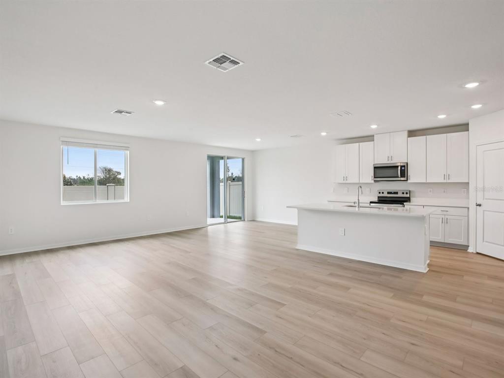 An open-concept kitchen and living area with white cabinets, a kitchen island, and light flooring — 10436 ABUNDANCE GROVE WAY, PARRISH, FL