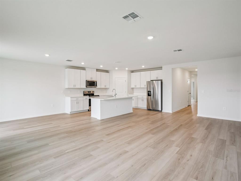 An open-concept kitchen features white cabinetry, stainless steel appliances, a center island, and wood-look flooring — 10436 ABUNDANCE GROVE WAY, PARRISH, FL