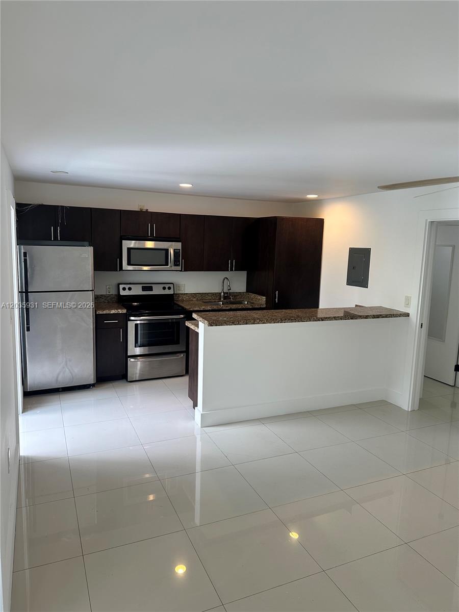 A kitchen features dark wood cabinets, stainless steel appliances, granite countertops, and white tile flooring — 3071 SW 27th Ave # 25, Miami FL 33133, MIAMI, FL