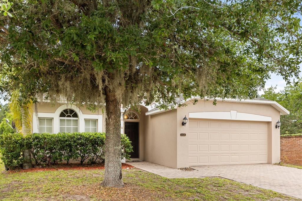 A single-story house with a beige stucco exterior, a two-car garage, and a large tree — 9406 CANDICE COURT, ORLANDO, FL