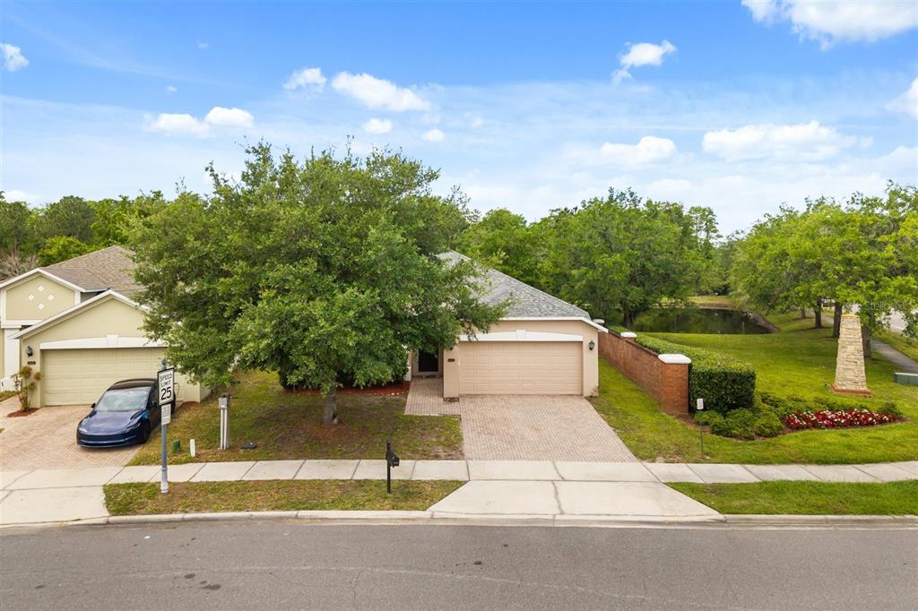 A single-story house with a two-car garage, a large tree, and a pond nearby — 9406 CANDICE COURT, ORLANDO, FL