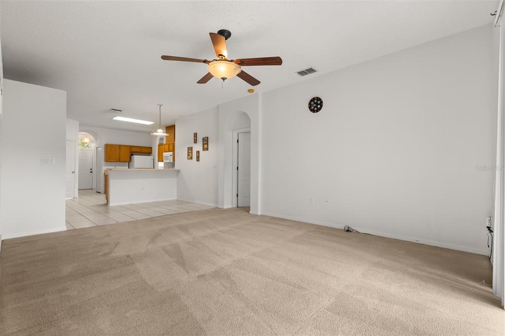 A carpeted living room features a ceiling fan and an open view into the kitchen — 9406 CANDICE COURT, ORLANDO, FL