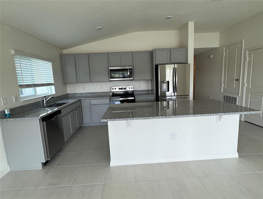 A kitchen features gray cabinets, granite countertops, stainless steel appliances, and a central island — 3815 PRONGHORN DRIVE, ST CLOUD, FL