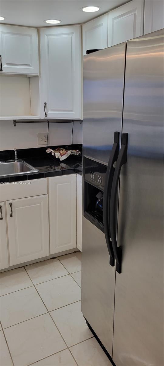 A kitchen features white cabinets, a black countertop, a stainless steel refrigerator, and tiled flooring — 13499 Biscayne Blvd # 511, North Miami FL 33181, NORTH MIAMI, FL