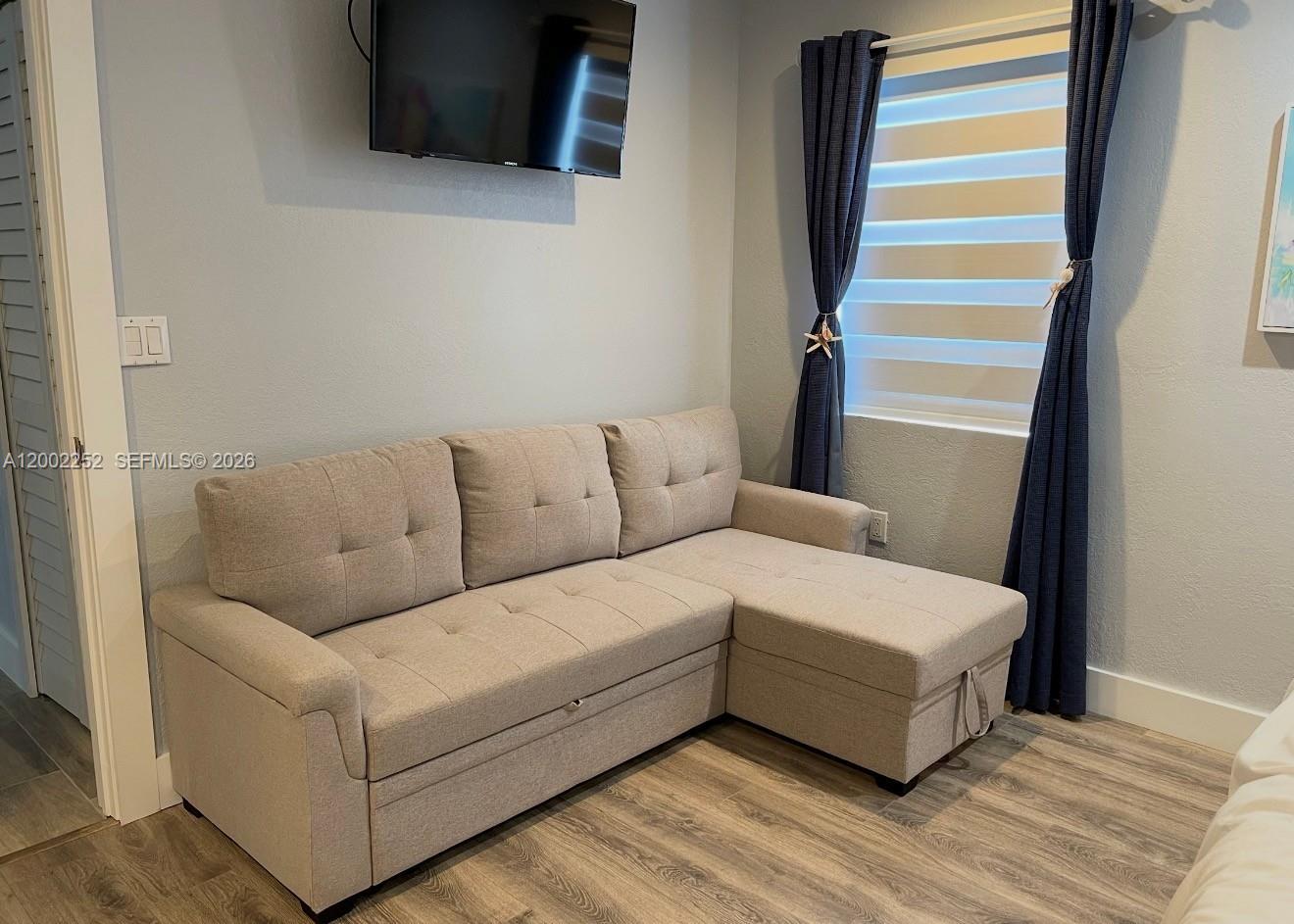 A light gray sectional sofa sits in a room with wood-look flooring and a television — 94825 Overseas Hwy 100, Key Largo FL 33037, KEY LARGO, FL