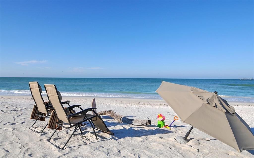 Two beach chairs and a tan umbrella sit on a sandy beach by the ocean — 8800 MIDNIGHT PASS ROAD, SARASOTA, FL