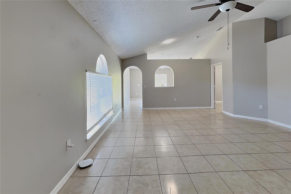 An empty room with beige tile flooring, vaulted ceilings, and arched wall openings — 11621 IVY FLOWER LOOP, RIVERVIEW, FL