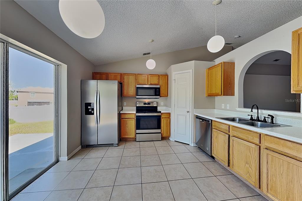 A kitchen with oak cabinets, stainless steel appliances, tile flooring, and a sliding glass door — 11621 IVY FLOWER LOOP, RIVERVIEW, FL