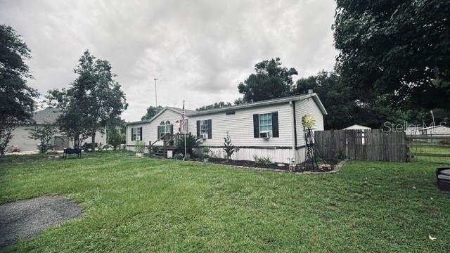 A single-story manufactured home with white siding sits on a grassy lot with a fence — 446 QUAIL STREET, LADY LAKE, FL