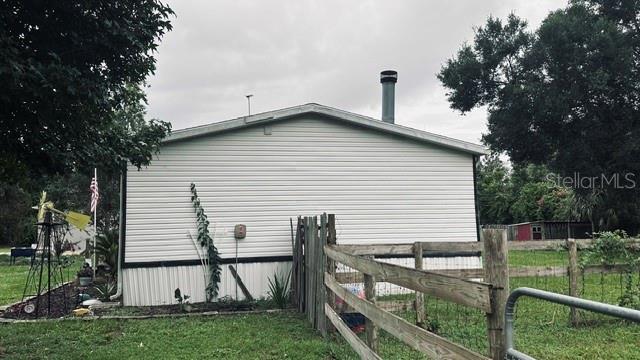 The exterior side of a white mobile home features a metal chimney and wooden fencing — 446 QUAIL STREET, LADY LAKE, FL
