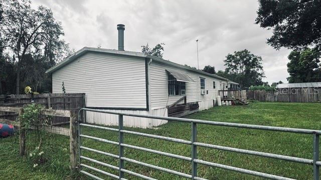 A white mobile home with a metal chimney stands behind a metal farm gate — 446 QUAIL STREET, LADY LAKE, FL