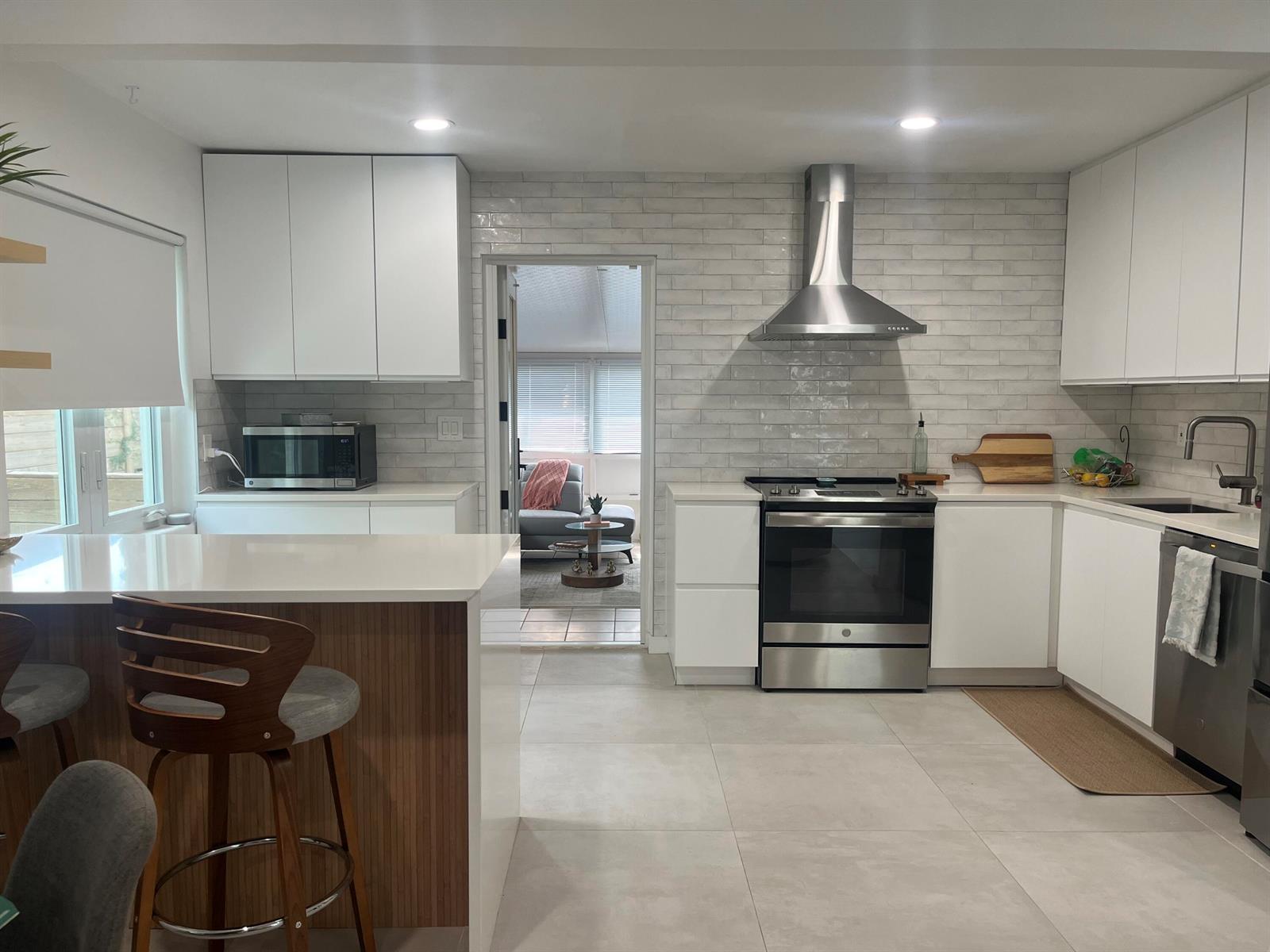 A modern kitchen features white cabinets, stainless steel appliances, a tiled backsplash, and a breakfast bar — 1612 N N Street, FL 33460, FL