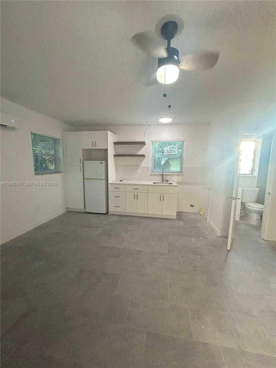 This kitchen features white cabinets, a refrigerator, open shelving, and gray tile flooring — 1220-1222 NE 110th Ter, Miami FL 33161, MIAMI, FL