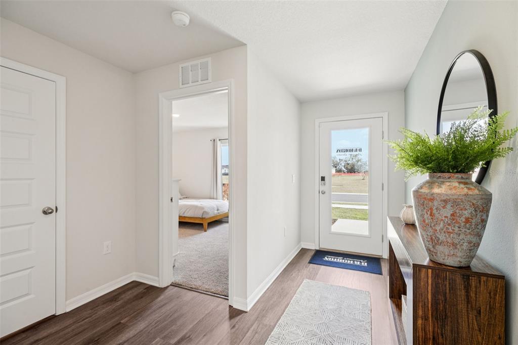 A bright entryway with wood-look flooring, a white front door, and a view into a bedroom — 4513 FAITH DRIVE, LAKE WALES, FL